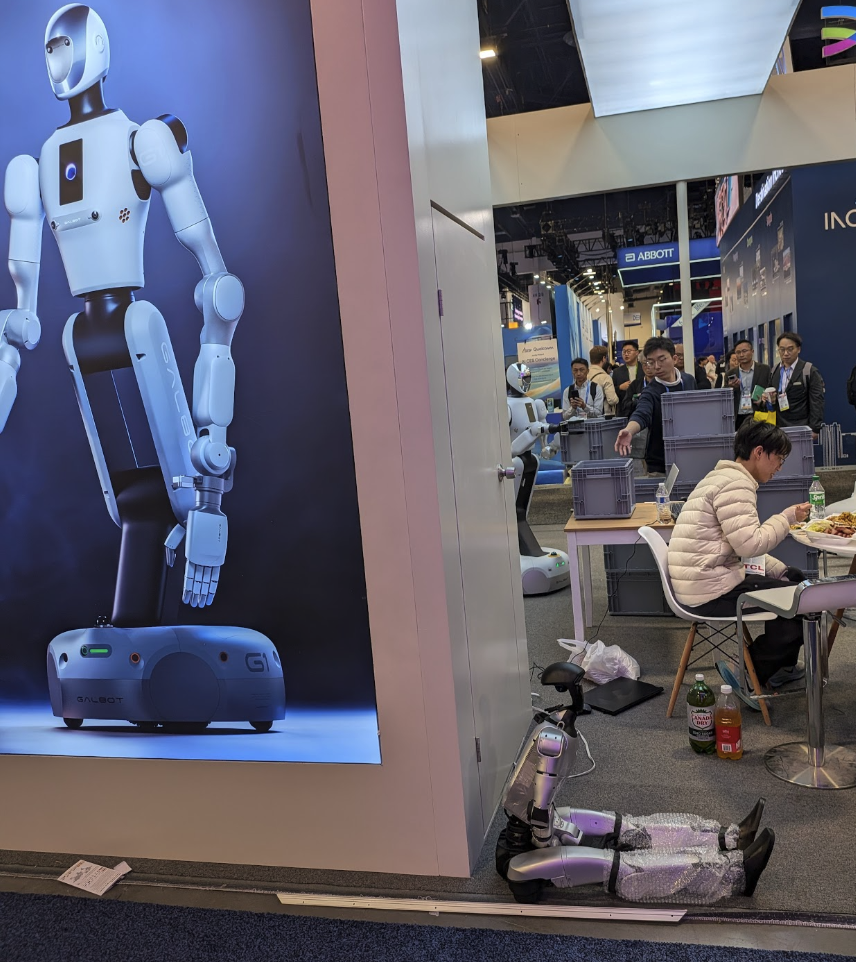 A little humanoid robot sitting on the floor, taking a break from the CES madness